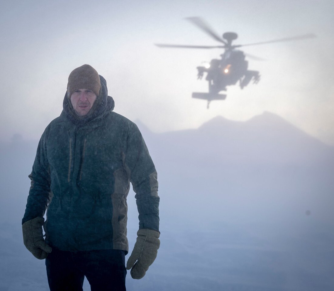 David Willetts standing in the snow at the Arctic Circle whilst an apache helicopter flies in the background.